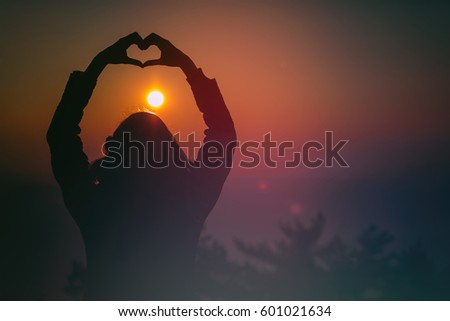 Silhouette of a girl making a heart-shape in nature.