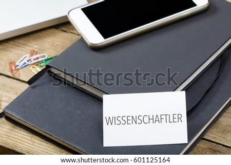 Wissenschaftler, German text for Scientist, business card on office desktop with notebooks, electronic devices, computer and phone.