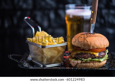 Burger, fried potatoes and beer on a dark background close-up. Street food. Fast food. Royalty-Free Stock Photo #601224983