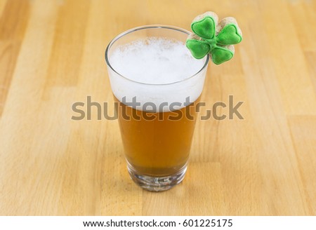Amber beer drink in a transparent glass with a high white foam and clover on a wooden base. The day of St. Patrick's Day.