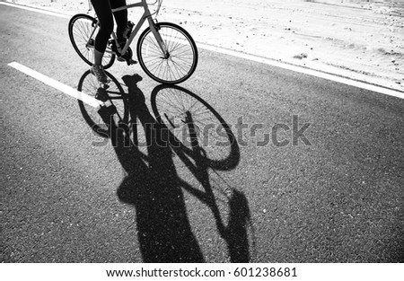 shadow of a woman riding bike on a road in desert. Black and white photograph
