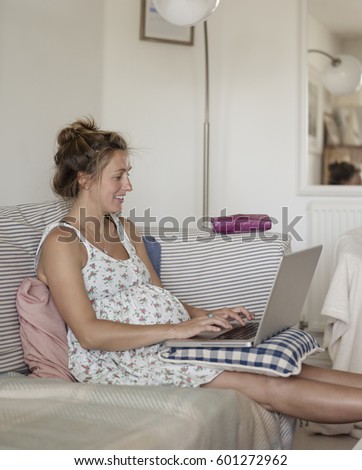 A pregnant woman seated on a sofa with her feet up