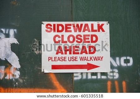 sidewalk closed ahead sign hanging on construction green wall in urban city