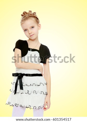 Beautiful little blonde girl dressed in a white short dress with black sleeves and a black belt.Girl poses for the camera.Close-up.On a yellow gradient background.