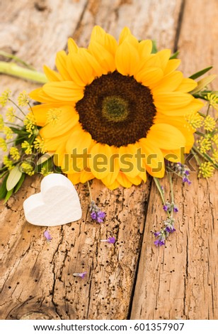 Rustic flowers bouquet with yellow sun flower and romantic white heart on wooden table.