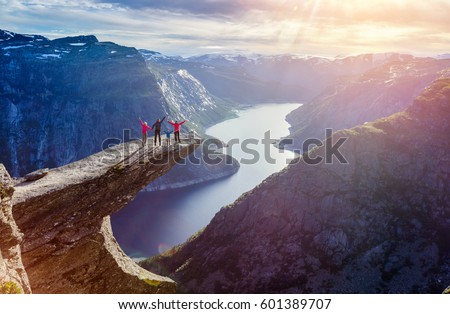 Happy Family On Trolltunga - View On Norway Mountain Landscape At Sunset From Trolltunga - The Troll's tongue in Odda, Ringedalsvatnet Lake, Norway. Royalty-Free Stock Photo #601389707