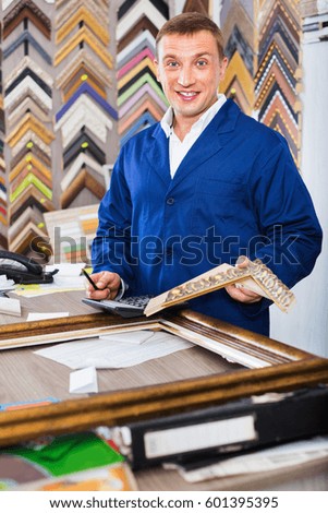 Smiling positive diligent man worker holding picture frame details on counter in studio 