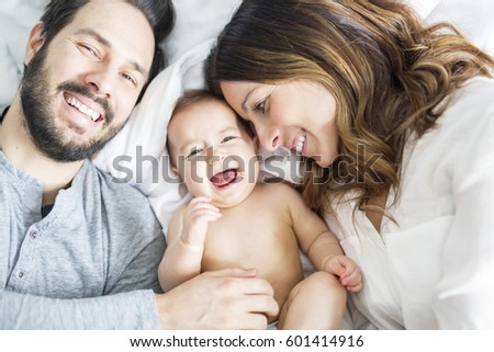 A Mother father and baby child on a white bed.