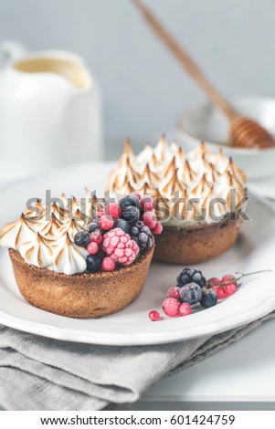 Two delicious tarts decorated with burned merengue and berries, served in white rustic composition