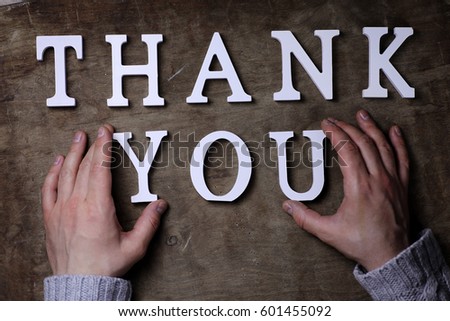 thank you word from white wooden letters on a table and hands 