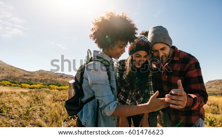 Three young hikers looking at pictures on mobile phone. Young people hiking in countryside.