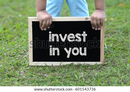 Toddler hold a blackboard with Invest in you text. 