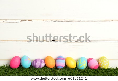 Easter Eggs, Colorful and Pretty, Laying in Grass in a Row against a Rustic and Distressed White Board Background with extra room or space for copy, text, your words or design.  It's a horizontal.