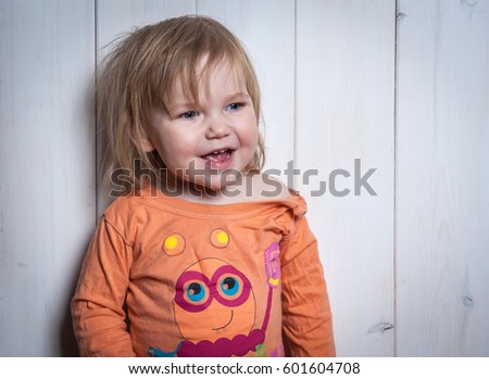 Cute smiling Toddler girl leaning against wooden wall. Educational toys for preschool and kindergarten child. Cute kids build toy railroad at home or daycare.