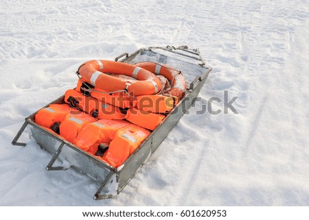 Orange life jackets and lifebuoys lying on a sled in the snow