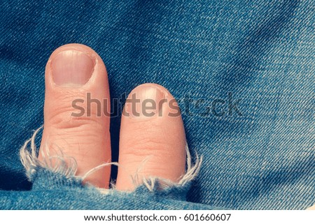 Two human fingers sticks out from a hole in jeans
