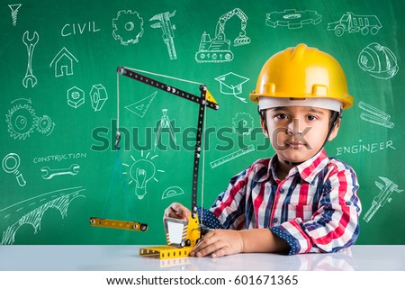 Cute little indian boy playing with toy crane wearing yellow construction hat or hard hat, childhood and education concept, with doodles drawn over green chalkboard