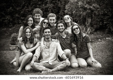 Group of young people sitting in the grass, they pose for the photo smiling. Black and white