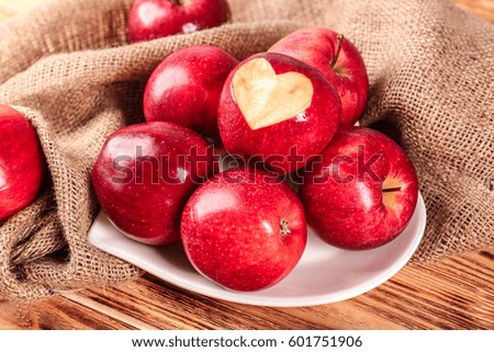 Plate in shape of heart with fresh red apples on wooden table