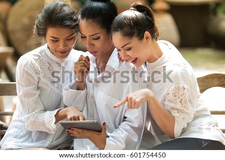 Group of three cheerful women sitting on a couch, They looking at the screen of a tablet.
