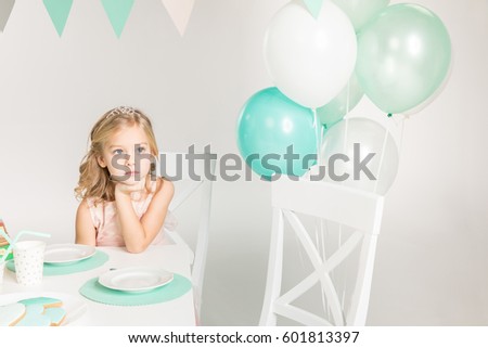 Adorable little girl sitting at birthday table and looking at balloons