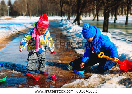 little boy and girl plaing with paper boats in spring puddle