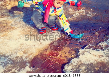 little girl plaing with paper boats in spring puddle