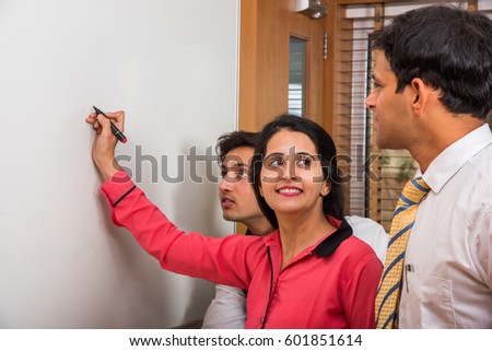 indian young businesswoman writing over white board with marker pen and other businesspeople looking
