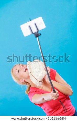 Technology, modern photography, confidence conept. Happy attractive adult blonde woman with sun hat taking funny picture of herself with smartphone on selfie stick.