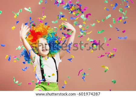 Brazilian Carnival. Venice Carnival. Little boy in clown wig jumping and having fun. Portrait of a child throws up a multi-colored tinsel and confetti. Birthday boy. Positive emotions.  Royalty-Free Stock Photo #601974287