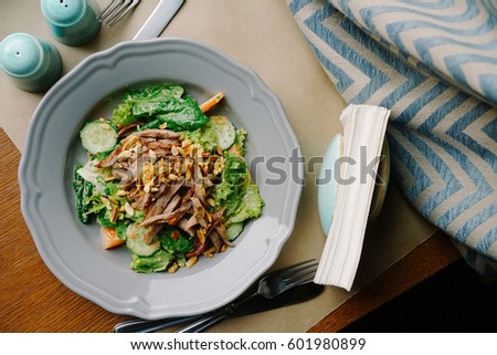 Picture of a place with fresh salad, napkins, salt and pepper.