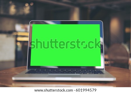 Mockup image of laptop with blank green screen on wooden table in vintage cafe
