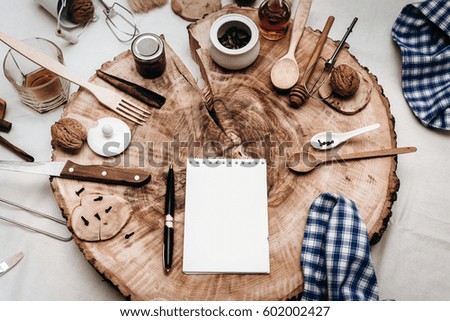 Notepad with a pen for recipes on a board of wood with wooden appliances spices of cloves, cinnamon, nut butter and cognac in glass. Brown tone concept photo for the kitchen. Space for text. Top view