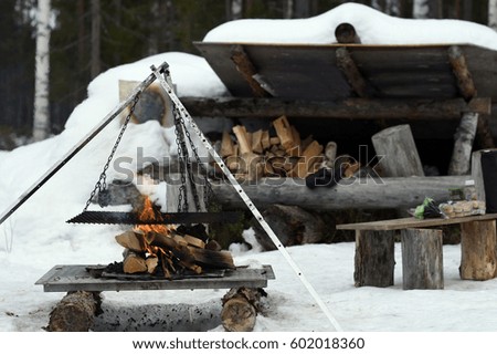 Construction for cooking in nature in winter with a burning fire and a hiking shelter in background picture from the Northern Sweden.