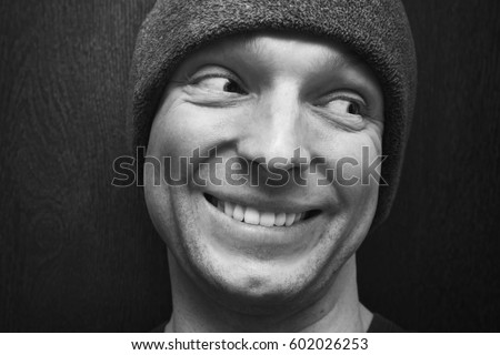 Young handsome smiling man in gray hat. Close-up studio face portrait over dark wooden wall background, selective focus, black and white photo