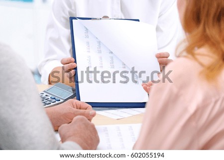 Middle aged couple signing contract at insurance agency office
