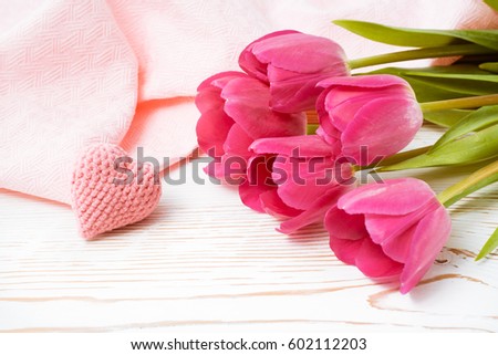 A bouquet of fresh pink tulips and a knitted heart on a wooden worn table