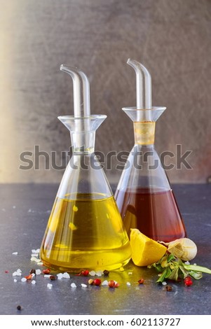 Grey abstract background with glass jars with olive oil and wine vinegar, lemon, garlic, sea salt, olive branch.  