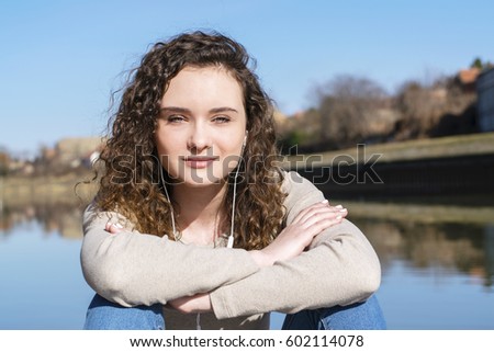 The girl listens to music next to the river