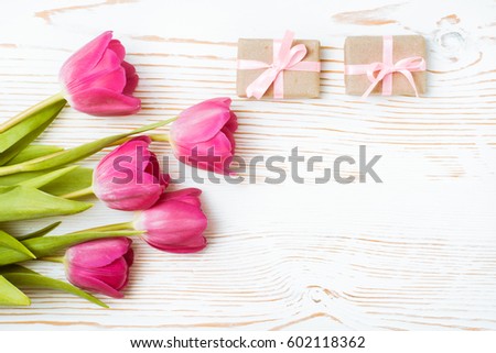 Bouquet of pink tulips and packaged gifts on a white wooden background. Top view. Flat composition