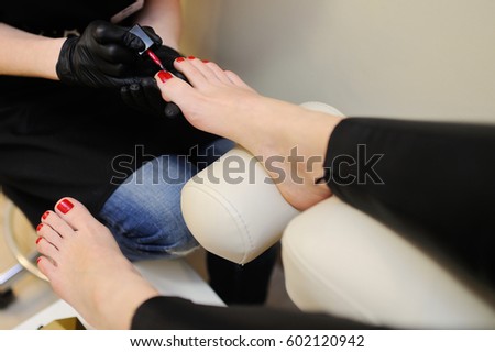 The nail wizard makes a pedicure to a girl. To paint nails in red color