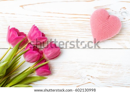 A bouquet of fresh tulips and a pink knitted heart on a white wooden background. Top view. Flat composition 