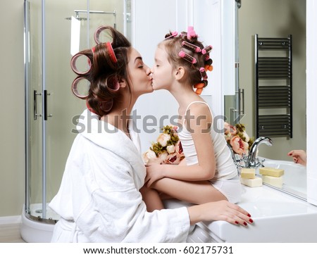 Young mother and daughter in curlers in a bath room happy smiling kissing girl family skin care concept in bathroom