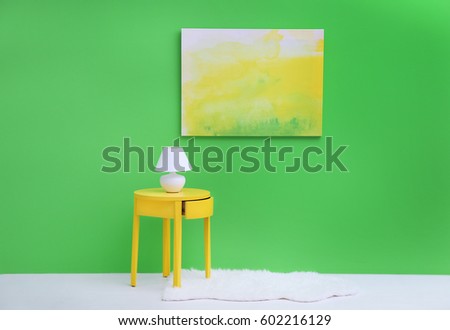 Lamp on little yellow table near green wall