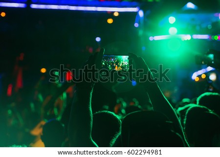 Video recording of the concert on the smartphone at the party. Silhouettes of concert crowd in front of bright lights on the background of a youth party.