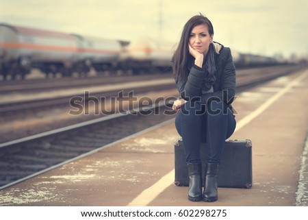 Cute woman at the train station, sitting on suitcase