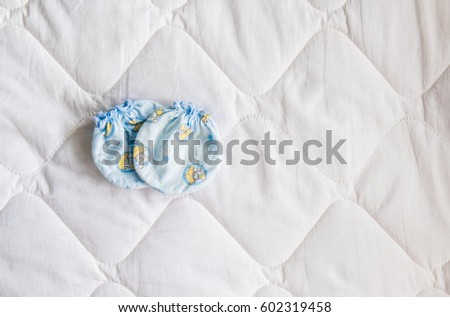 Above view of mittens for a newborn baby on a white blanket in the bedroom. Gloves for the infant put on the bed with copy space. Top-down