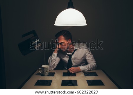The man is sitting at the table in dark room with lamp. He is tired. The kettle is hanging near him and pouring hot water by itself in a white cup. Great unreal creative photo.
