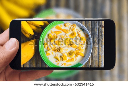 Healthy breakfast concept. Taking picture of cornflakes with milk, banana and mango with mobile phone. Phone in male hands. Top view, vintage style. Wooden bamboo background.
