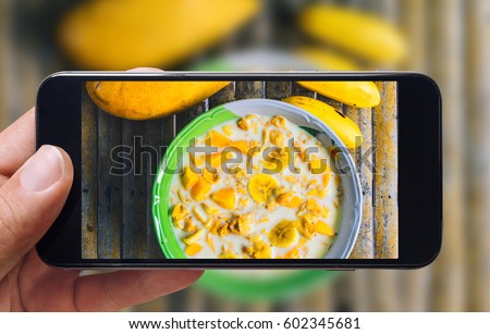 Healthy breakfast concept. Taking picture of corn flakes with milk, bananas and mango with mobile phone. Phone in male hands. Vintage style.Rusty bamboo background.